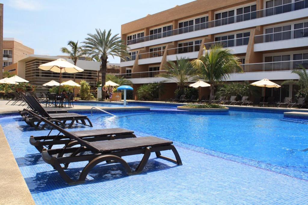 PampatarHotel Margarita Real的酒店旁的游泳池配有椅子和遮阳伞
