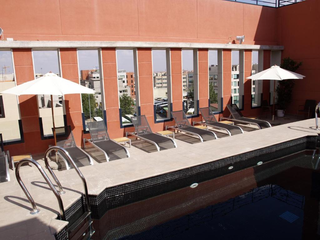 马德里阿尔卡拉套房生态酒店的大楼内一个带椅子和遮阳伞的游泳池