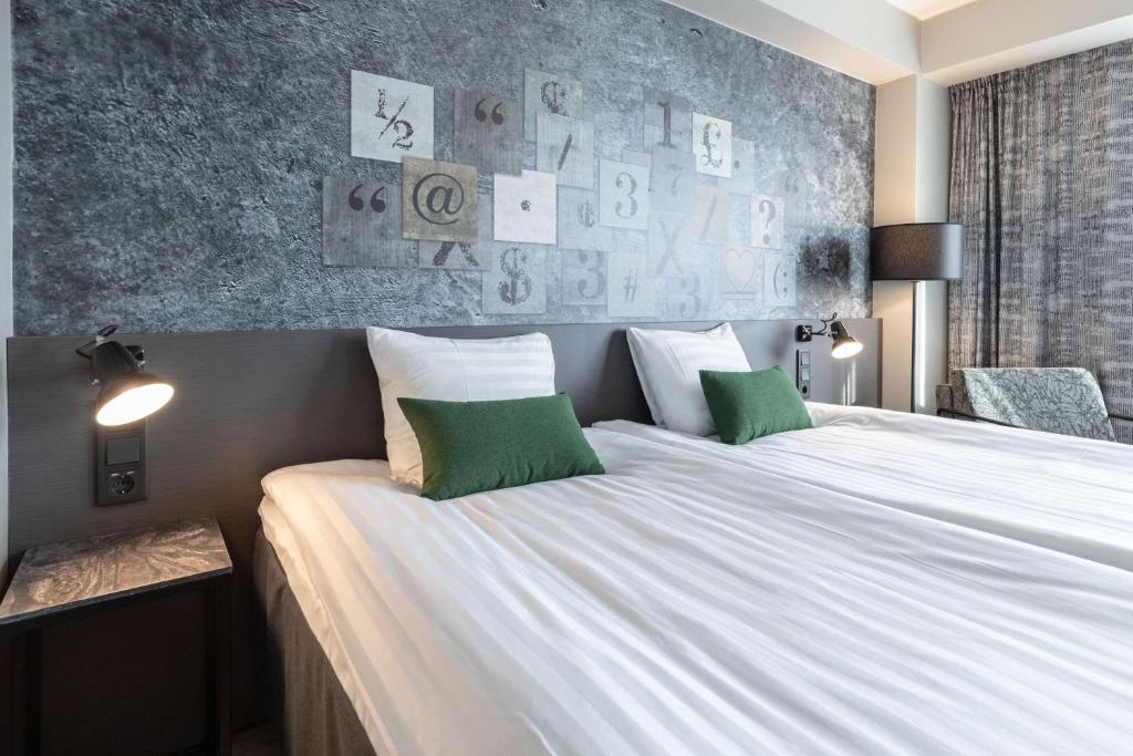 赫尔辛基斯甘迪克卡里奥酒店的卧室配有一张带两个绿色枕头的大型白色床