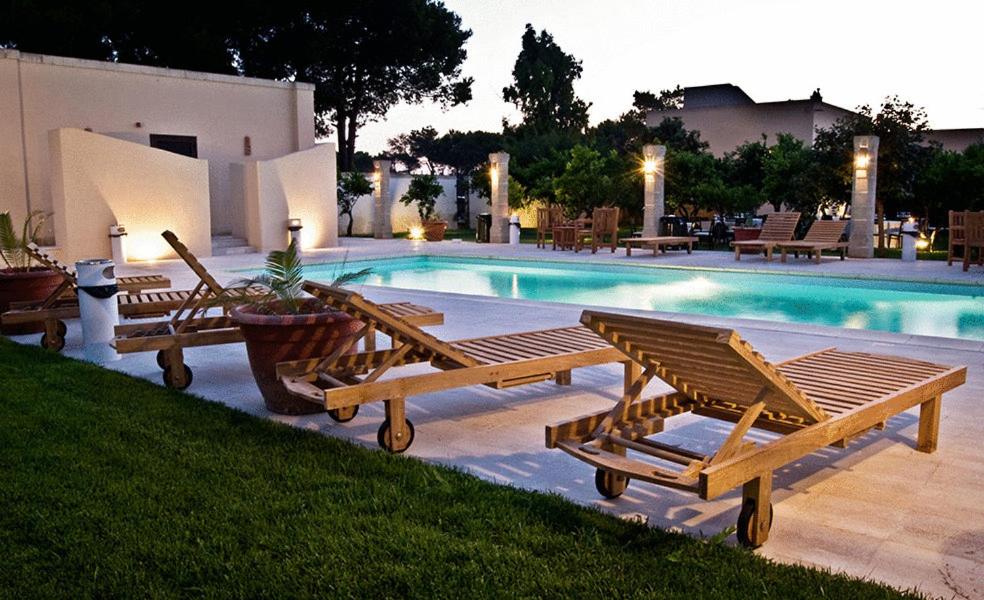 莱切省卡瓦利诺Masseria Li Campi的一组木制长椅,毗邻一个游泳池
