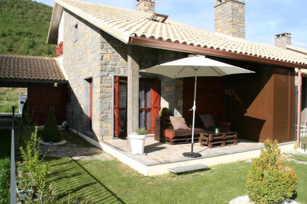 加文Casa Rural Biescas en el Pirineo的一座带遮阳伞和椅子的小石头房子