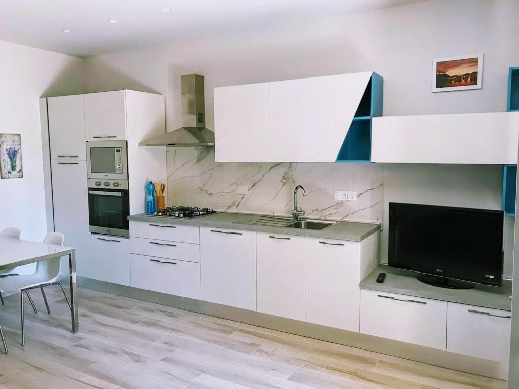 莱里奇Residence Mare Azzurro的厨房配有白色橱柜、电视和桌子。