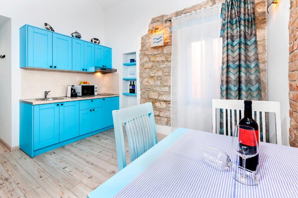 罗维尼Apartments & Rooms La casa Barbaro的厨房配有蓝色橱柜和1张带1瓶葡萄酒的桌子