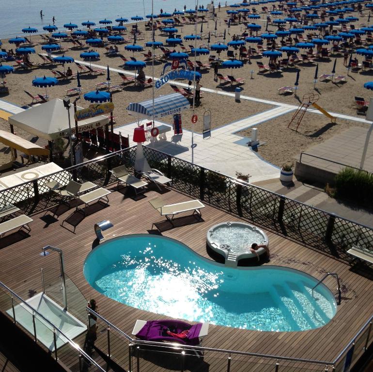 里米尼拜亚酒店的游泳池以及带椅子和遮阳伞的海滩