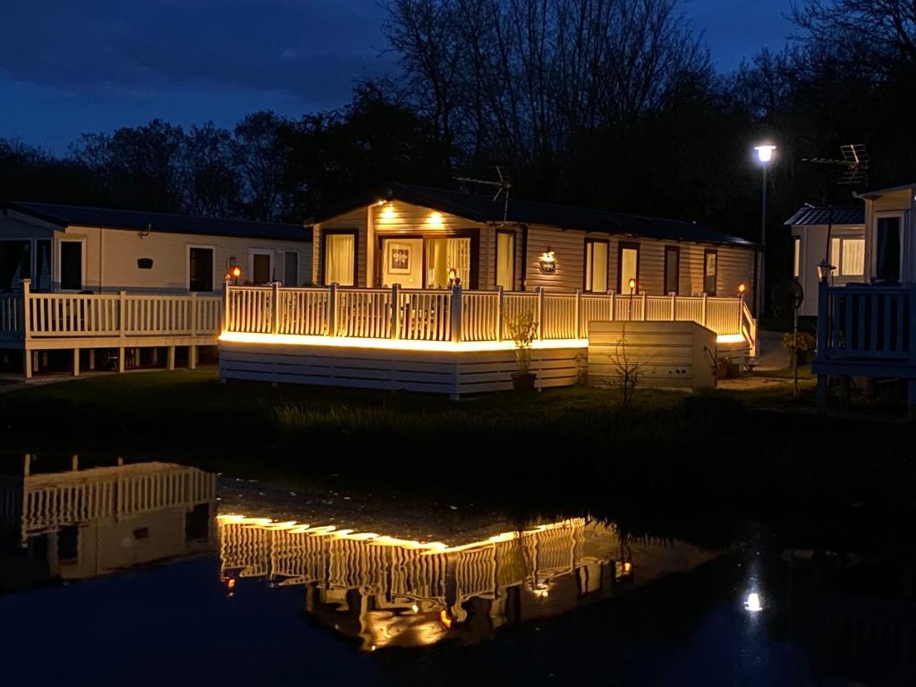 赛伦塞斯特Auroras Dream Lodge - Hoburne Cotswolds Holiday Park的夜晚水灯的房子