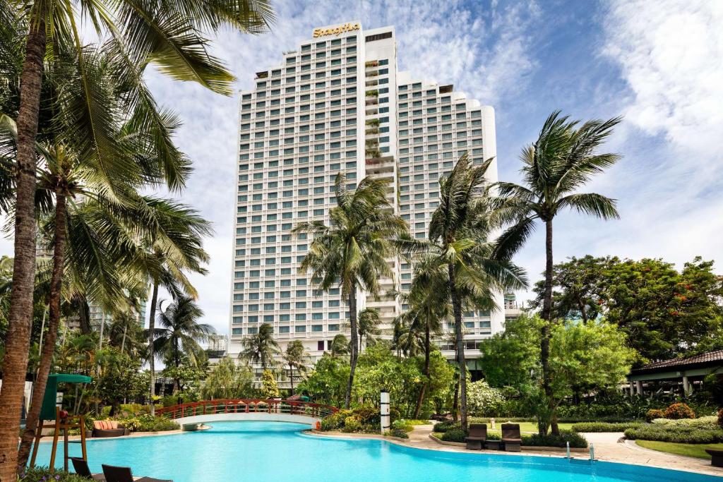 雅加达Shangri-La Jakarta的一座高大的建筑,在游泳池前种有棕榈树