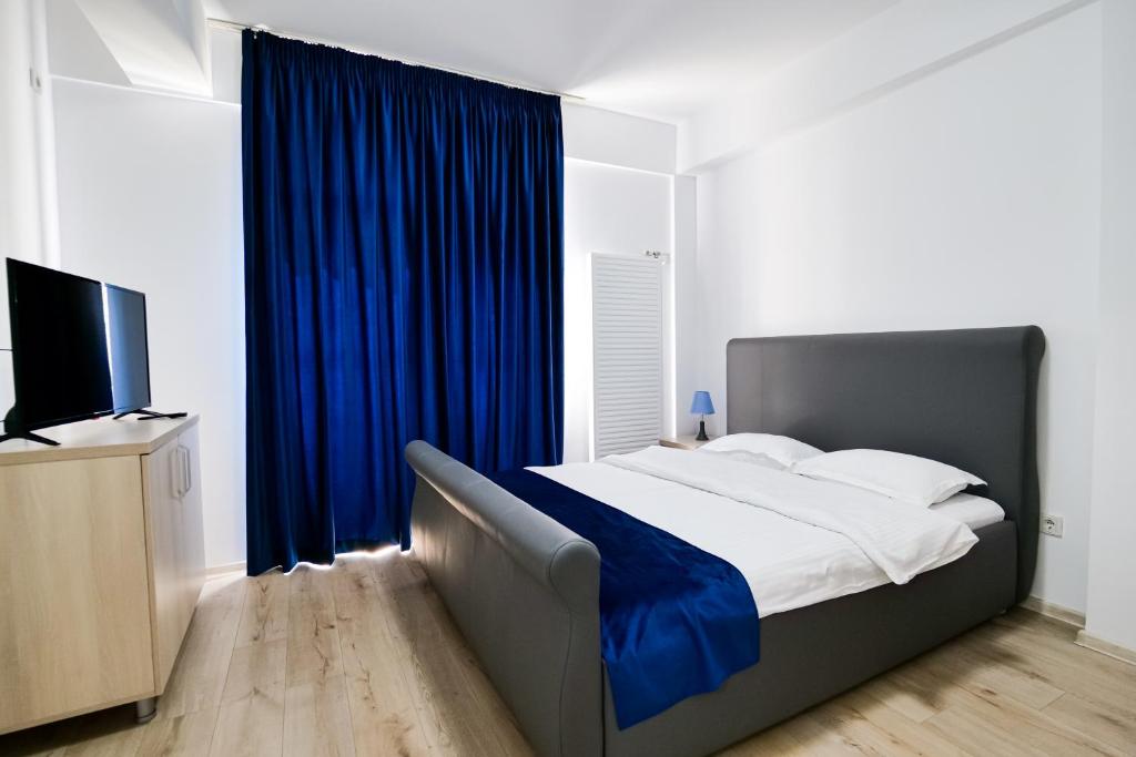 布加勒斯特Hotel Ema&Zain的一间卧室配有一张带蓝色窗帘的床和电视。