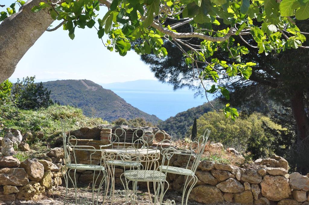 Capo D'ArcoFerienhaus Elba Porto Azzurro mit Panorama und Garten的一张桌子和椅子,坐在岩石墙的顶部