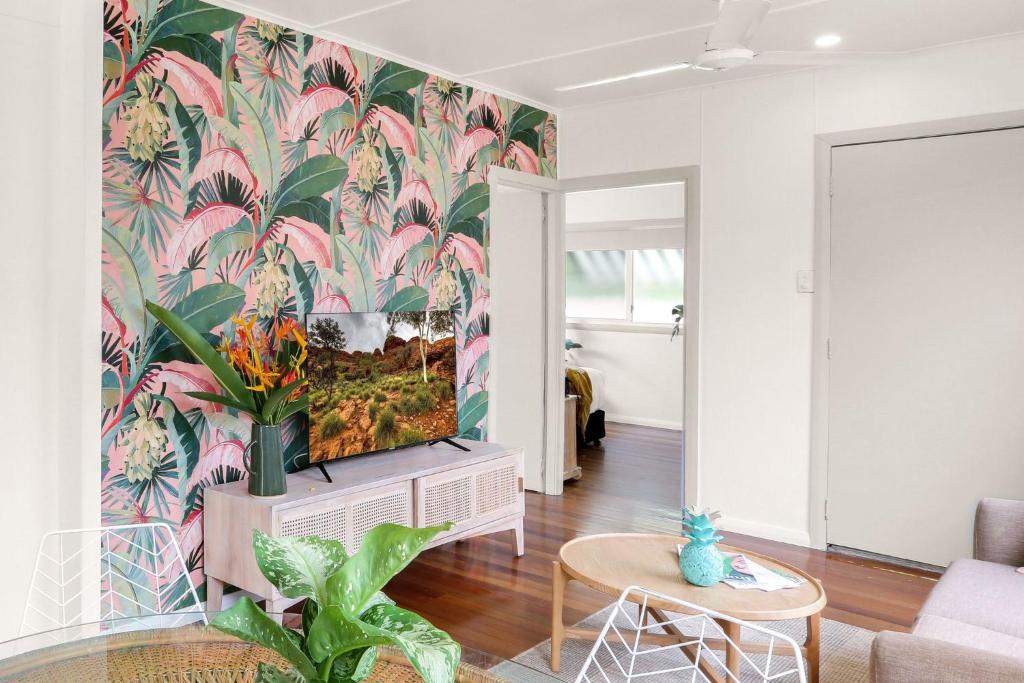 Cairns NorthTropicana Bungalow - Retro Getaway的客厅的墙上设有电视,墙上装饰着热带壁纸