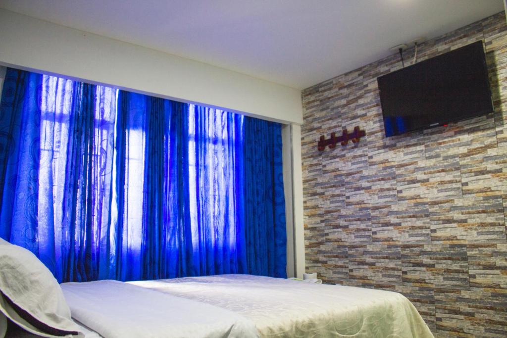波哥大Hotel Punto 100的一间设有蓝色窗帘的卧室和砖墙上的电视