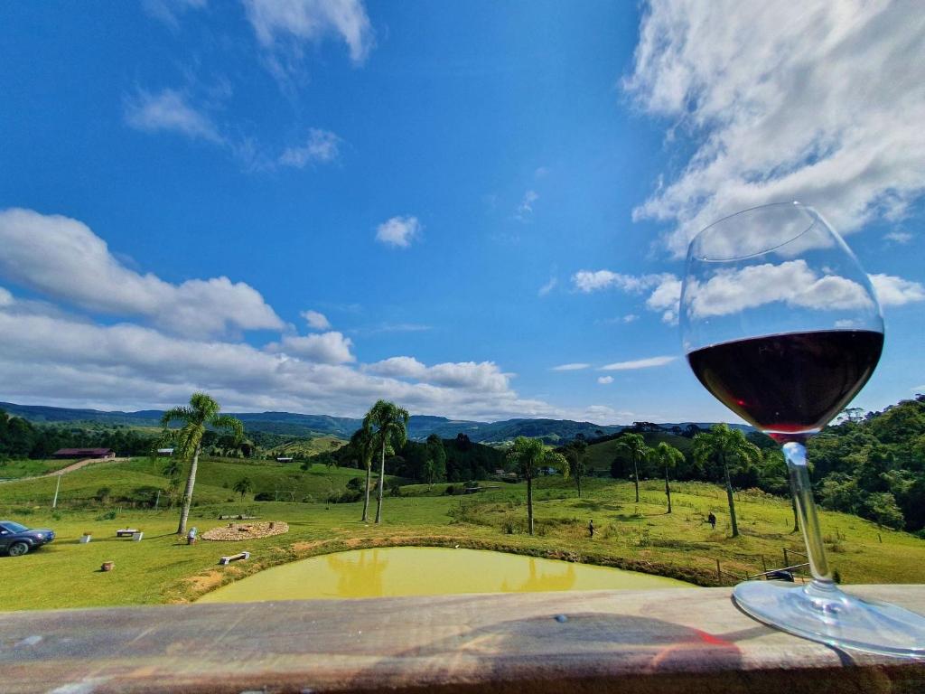 兰舒凯马杜Cabana Pôr-do-Sol - Rancho Queimado/SC的坐在桌子上一边欣赏田野美景一边享用一杯葡萄酒
