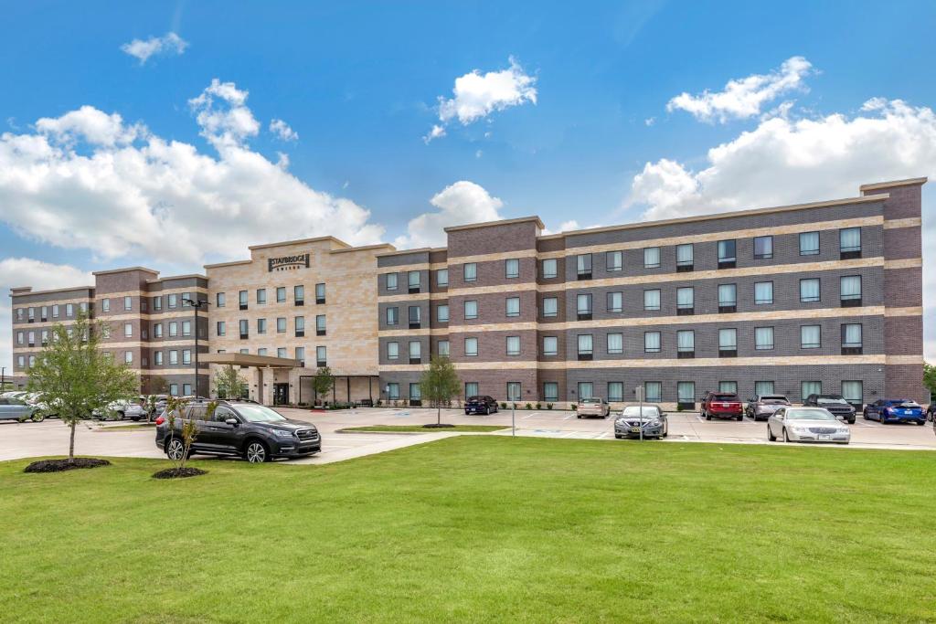 大草原城Staybridge Suites Grand Prairie Near Epic Central, an IHG Hotel的停车场内停放汽车的大型建筑