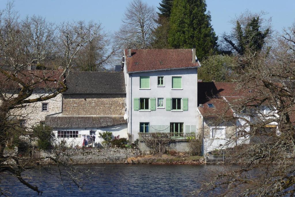 Peyrat-le-ChâteauChambres d'Hôtes L'Hirondelle du Lac的一条大白色房子,有绿色百叶窗,毗邻河流