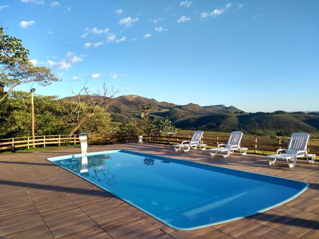 圣罗克迪米纳斯Pousada Capão Fôrro的一个带椅子的游泳池和一个背景为山脉的甲板
