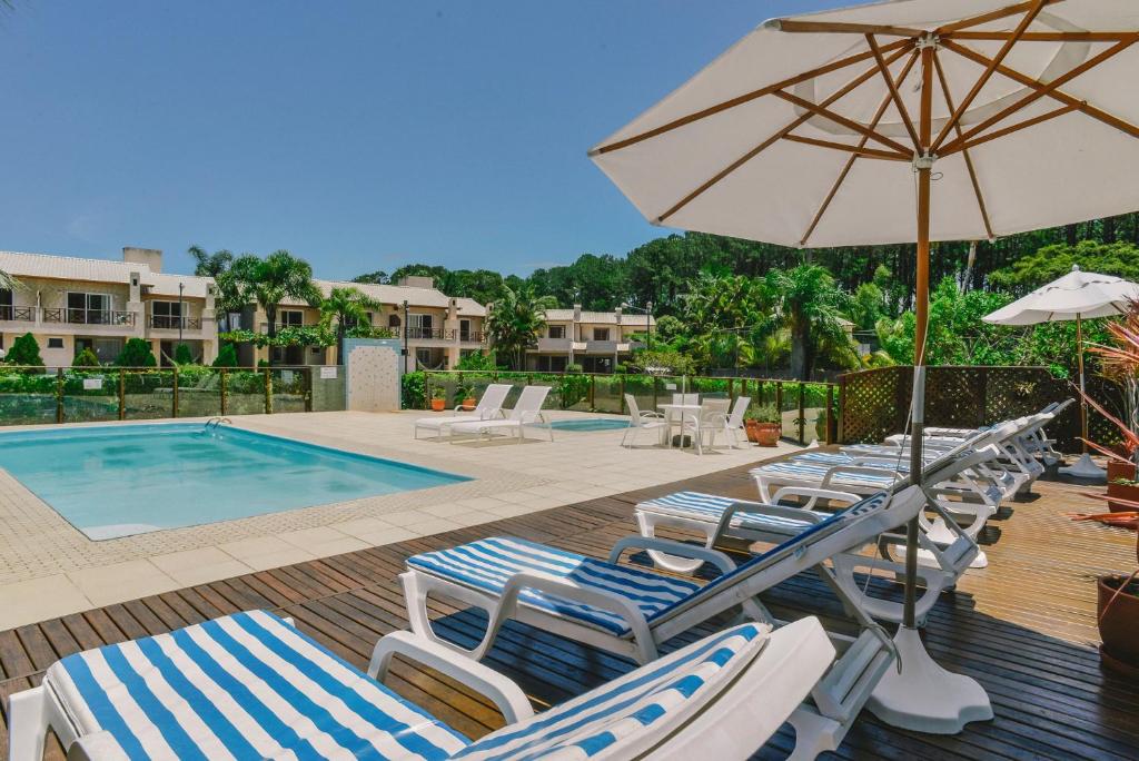 弗洛里亚诺波利斯Villa Oliva Residence的一组躺椅和一把遮阳伞,位于游泳池旁