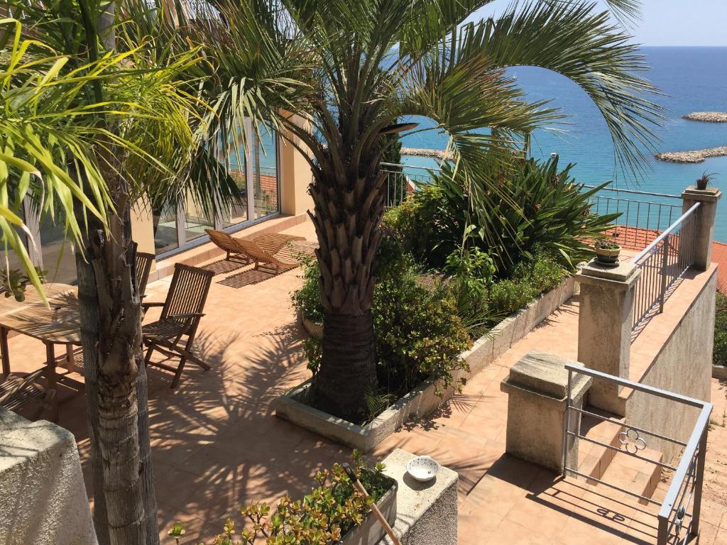 芒通Villa l'ensoleillée vue panoramique mer, 250 m de la plage et du centre ville的一个带椅子和棕榈树的庭院和大海