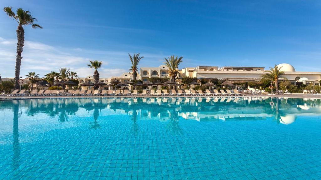 米多恩Djerba Aqua Resort的一个带椅子和棕榈树的大型蓝色游泳池