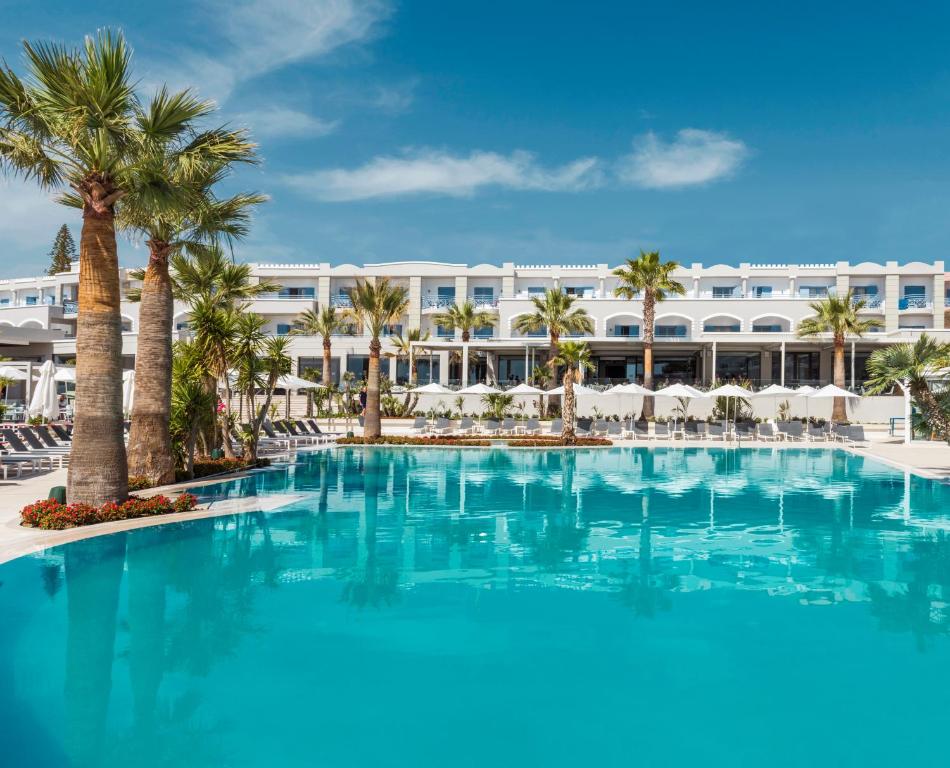 吉奥塔略Mitsis Rodos Village的一座棕榈树的大型游泳池,以及一间位于酒店后面的酒店