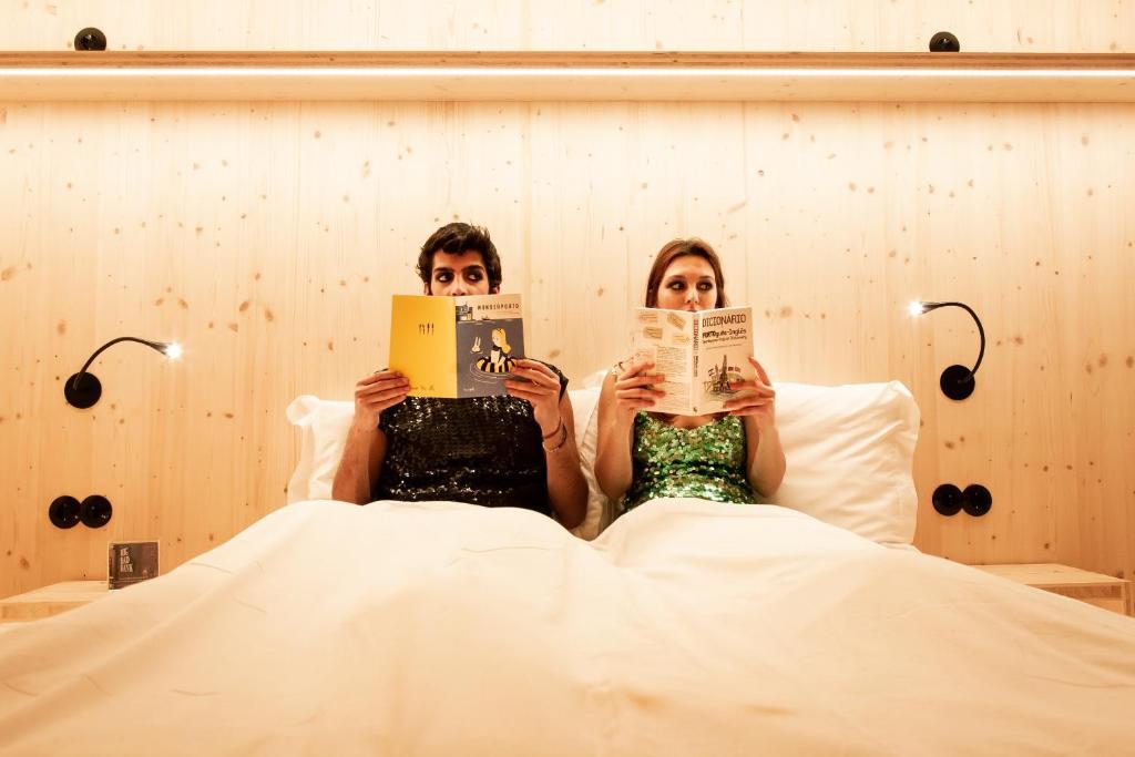 波尔图Zero Box Lodge Porto的躺在床上看书的男人和女人