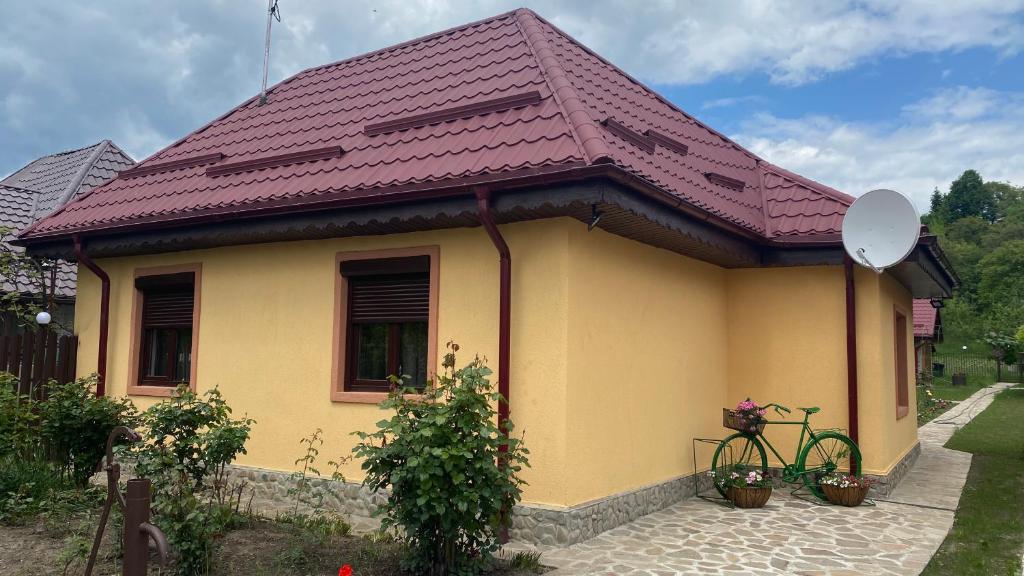 AlmaşCasa de vacanta - Ograda cu flori的黄色房子,带一辆自行车,屋顶紫色