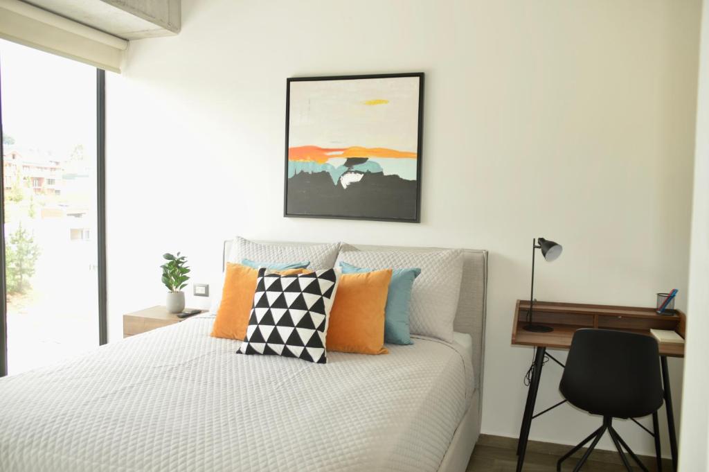 危地马拉Cozy Stays Cayala Apartments 5的一间卧室配有一张带橙色枕头的床和一张书桌