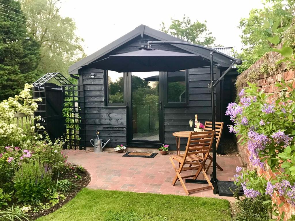 朗梅尔福德Melford Allotment Shed-Vintage Lodge Suffolk的黑色棚子,带桌子和雨伞