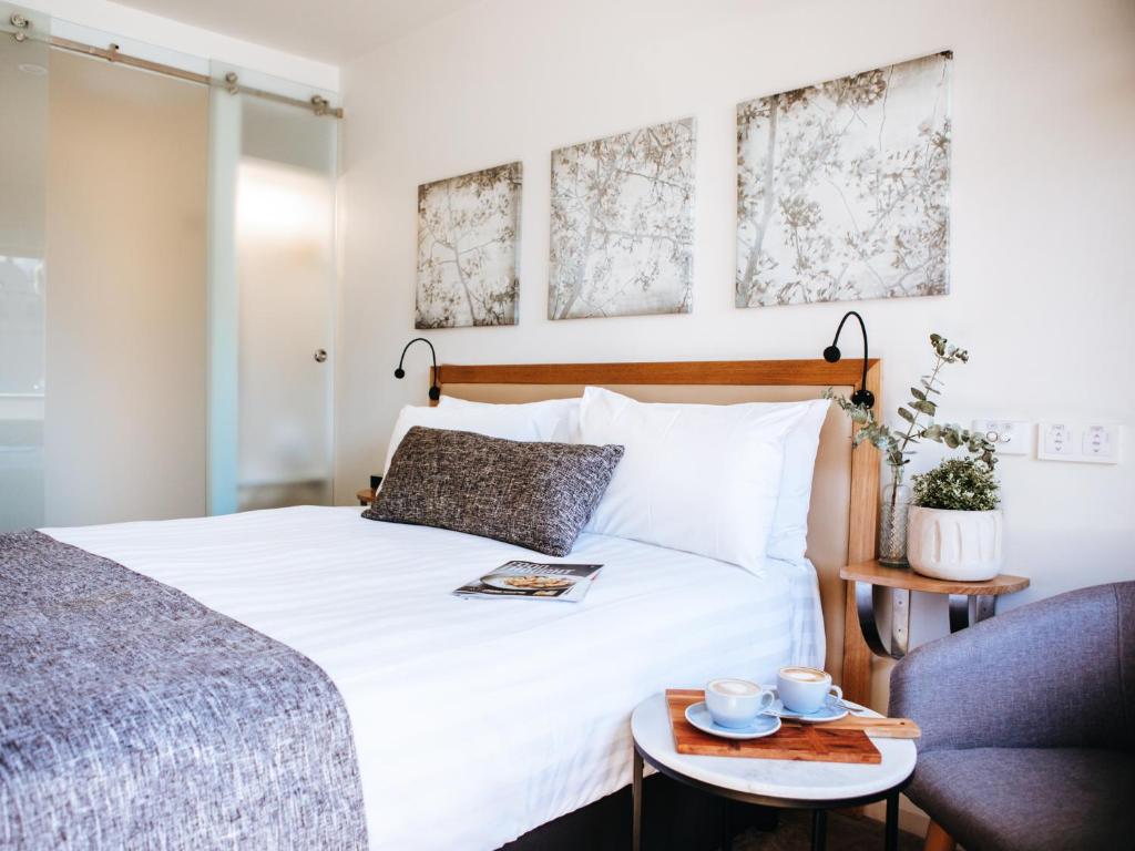 沃加沃加阿斯特酒店的卧室配有白色的床和带杯子的桌子。