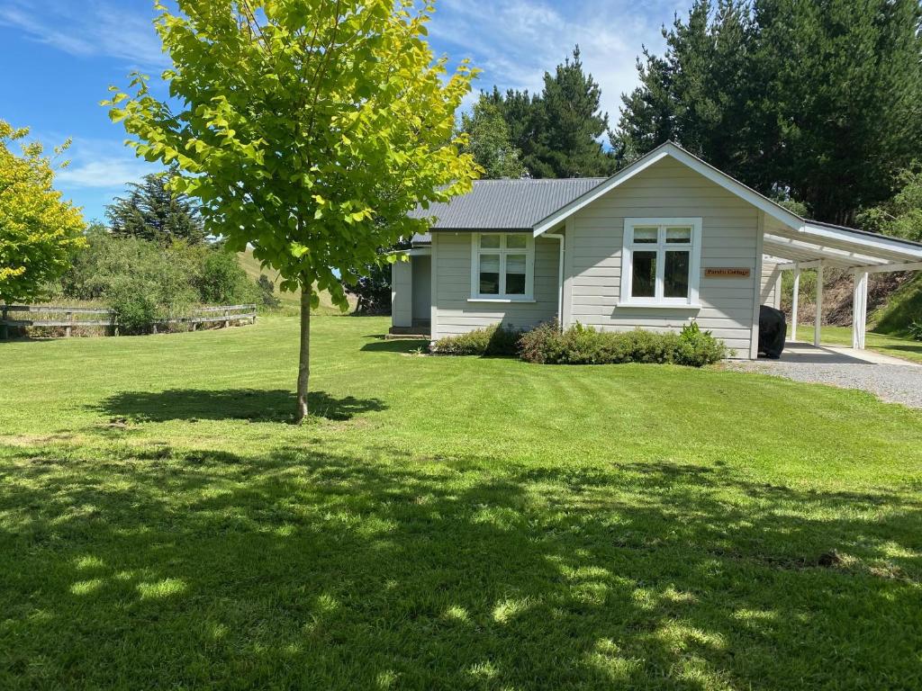  WaipukurauParatu Farm Cottage in a quiet rural setting.的院子中一棵树的小白色房子