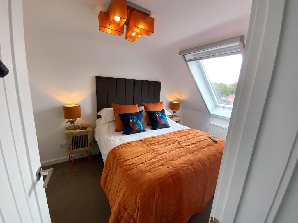 利明顿THE HIDEAWAY - LUXURY SELF CATERING COASTAL APARTMENT with PRIVATE ENTRANCE & KEY BOX ENTRY JUST A FEW MINUTES WALK TO THE BEACH, SOLENT WAY WALK, SHOPS and many EATERIES & BARS - FREE OFF ROAD PARKING,FULL KITCHEN, LOUNGE,BEDROOM , BATHROOM & WI-FI的一间卧室配有带橙色床单的床和窗户。