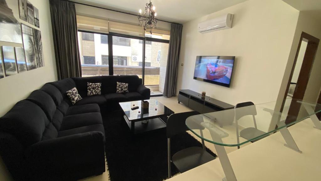 安曼Dair Ghbar Apartment的客厅配有黑色沙发和玻璃桌