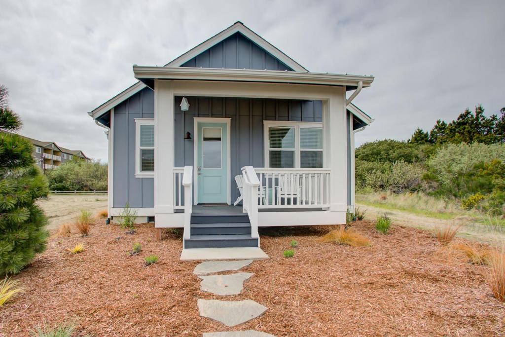 洋滨市Sand Castle Cottage - Oyhut Bay Seaside Village的蓝色的小房子,设有门廊和椅子