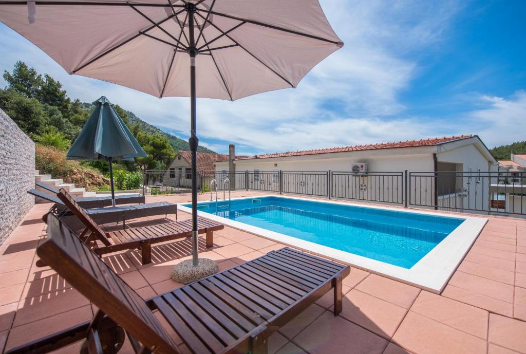 德尔韦尼克Apartmani Petracie的一个带遮阳伞和长凳的游泳池以及一个游泳池