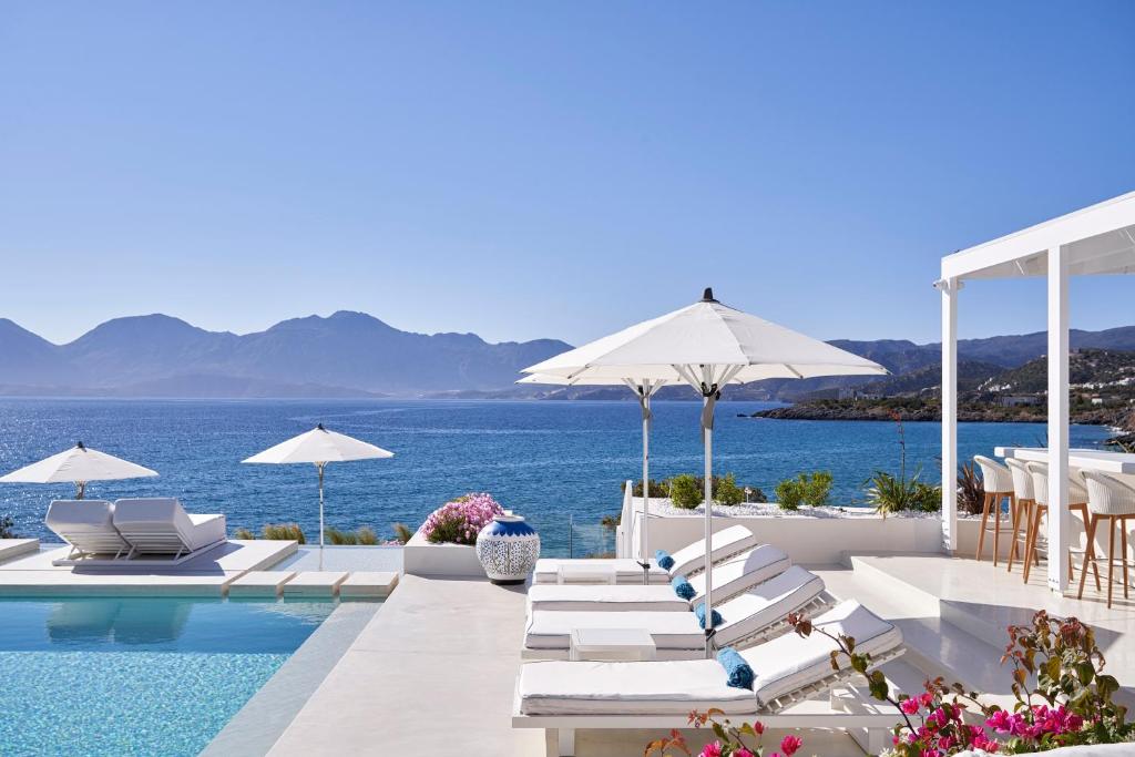 阿基欧斯尼古拉斯The Island Concept Luxury Boutique Hotel Heated Pool的一个带椅子和遮阳伞的游泳池以及大海