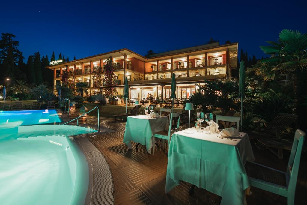 加尔达Villa Madrina Lovely and Dynamic Hotel的一个带桌子的度假胜地,晚上设有游泳池