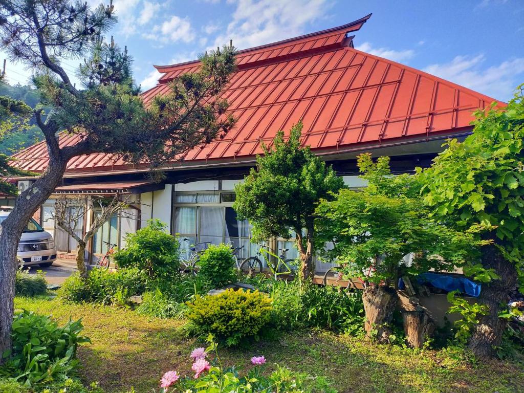 中野市Madarao Farm的一座有红色屋顶、一些树木和花卉的房子