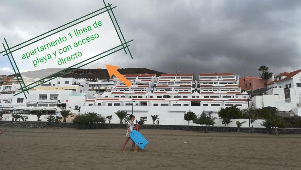洛斯克里斯蒂亚诺斯Apartamento en Los Cristianos的一名妇女带着蓝色冲浪板在海滩上行走