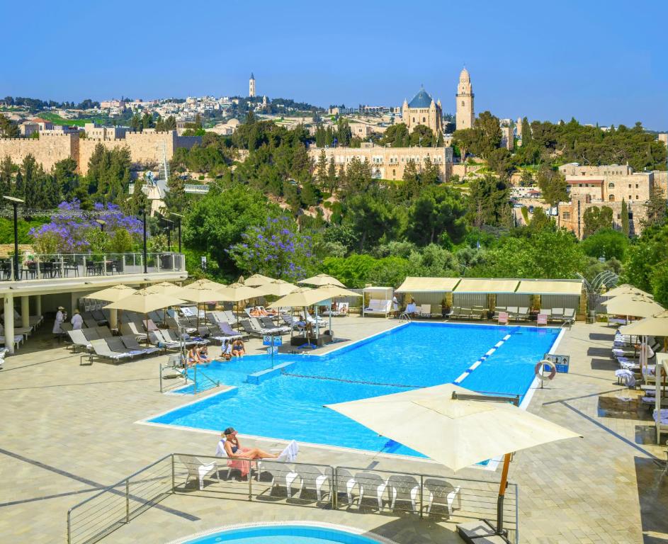 耶路撒冷耶路撒冷因巴尔酒店的一座带遮阳伞的游泳池以及一座城市