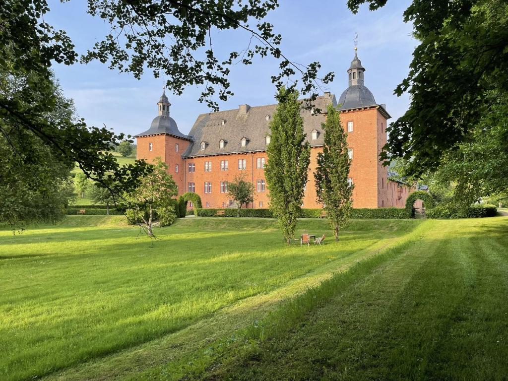 基希洪德姆Ferienwohnungen Jagdschloss Adolphsburg的一座大红砖建筑,在田野里种有树木