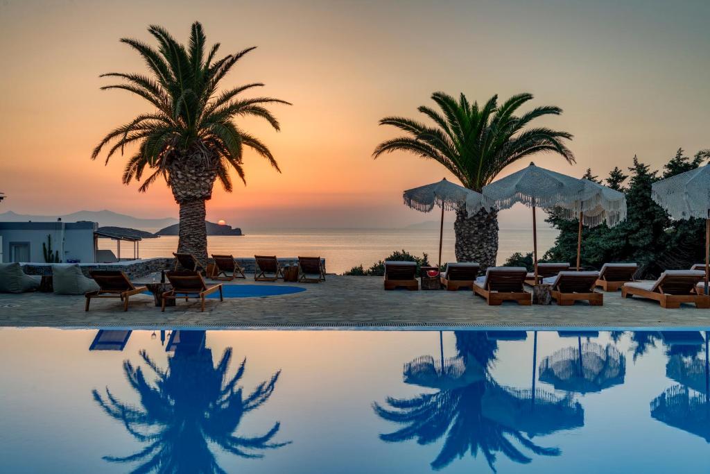 阿佐里姆诺斯法罗斯度假村 的棕榈树和椅子的游泳池以及日落