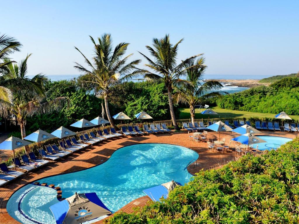 UmzumbePumula Beach Hotel的一个带游泳池、椅子和棕榈树的度假村