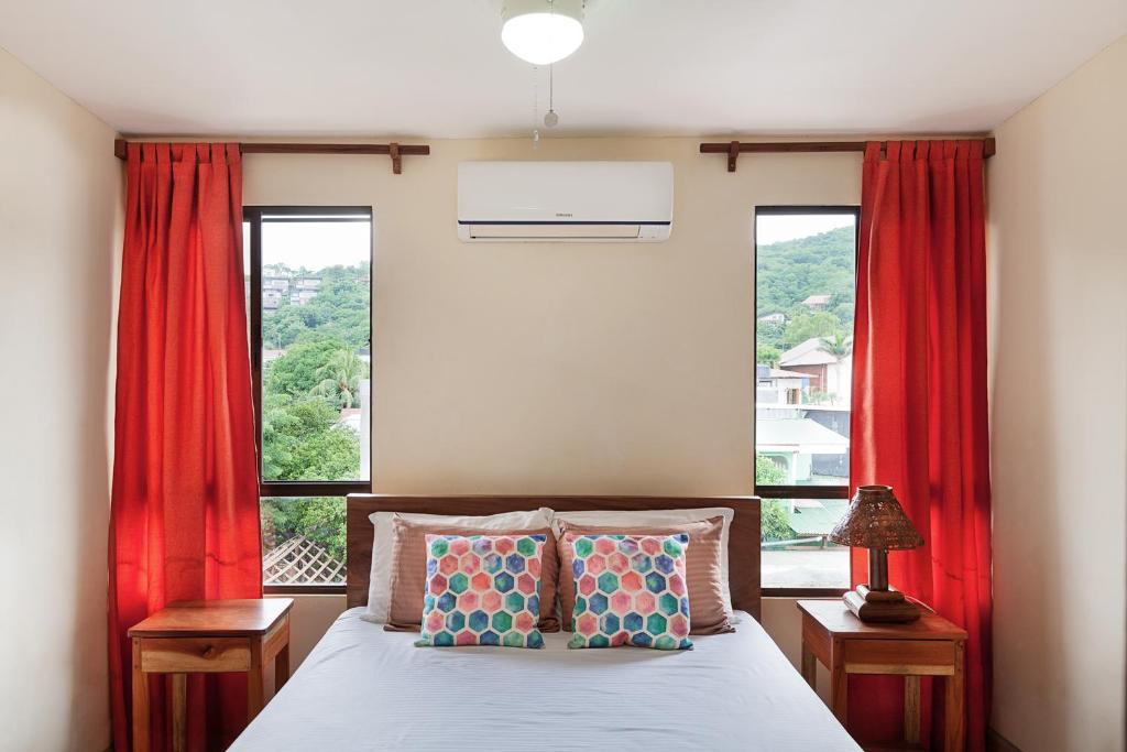 南圣胡安Hostel Tropical and CoWorking的一间卧室配有床和两个带红色窗帘的窗户。