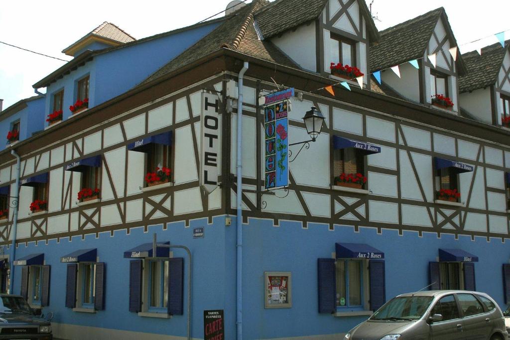 新布里萨克Hôtel Restaurant Aux Deux Roses的一座蓝色和白色的建筑,前面有停车位