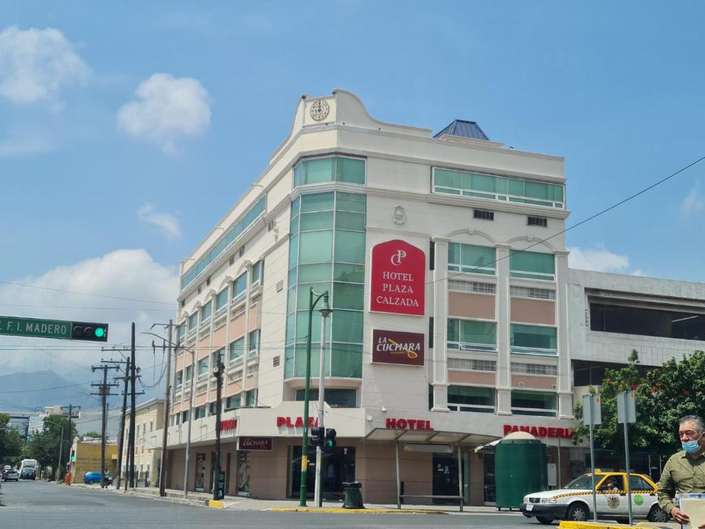 蒙特雷Hotel Plaza Calzada的白色的建筑,旁边有一个红色的标志