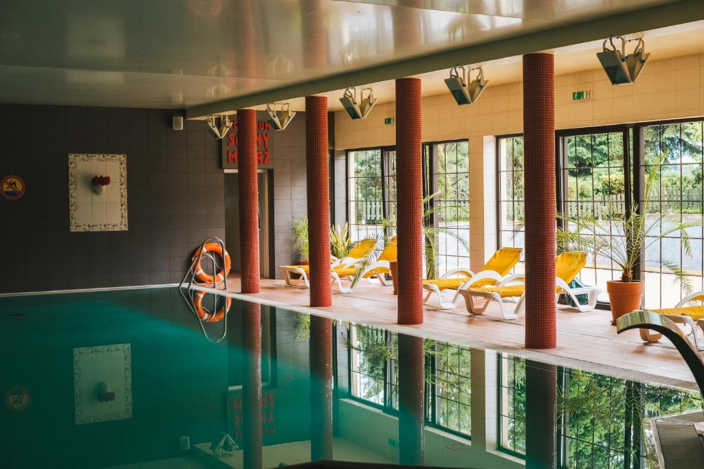 梅斯瓦科维采查塔扎维希亚酒店的游泳池设有黄色的椅子和桌子以及窗户。