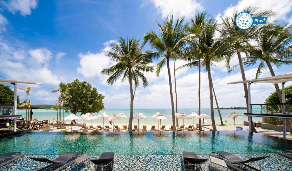 查汶Sareeraya Villas & Suites的一个带椅子和棕榈树的游泳池以及大海