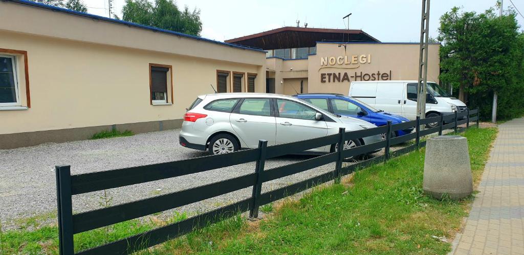 热舒夫ETNA - Hostel -Noclegi Rzeszów的两辆汽车停在大楼前的围栏旁边