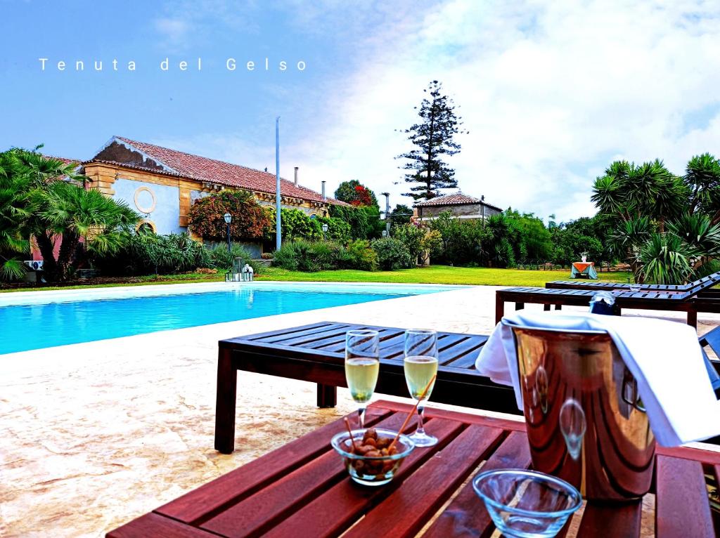 卡塔尼亚Tenuta del Gelso的一张桌子,旁边是游泳池,上面有两杯葡萄酒