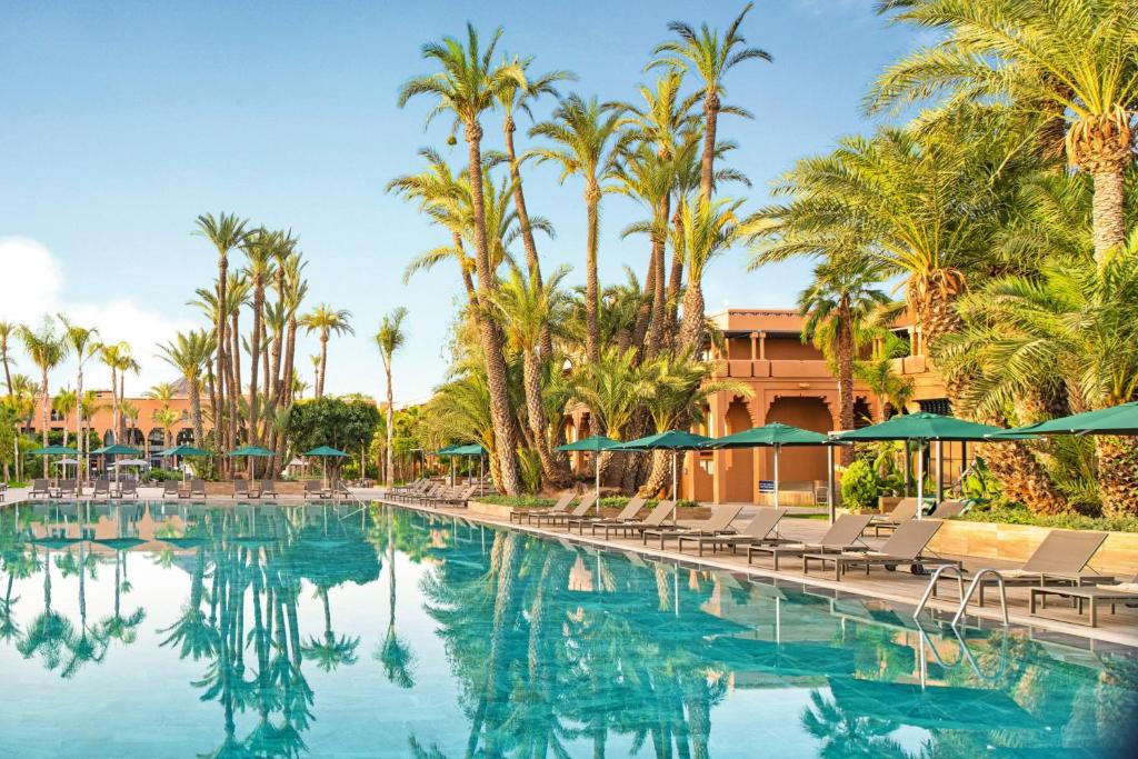 马拉喀什Hotel Riu Tikida Garden - All Inclusive Adults Only的一个带椅子和遮阳伞的游泳池以及棕榈树