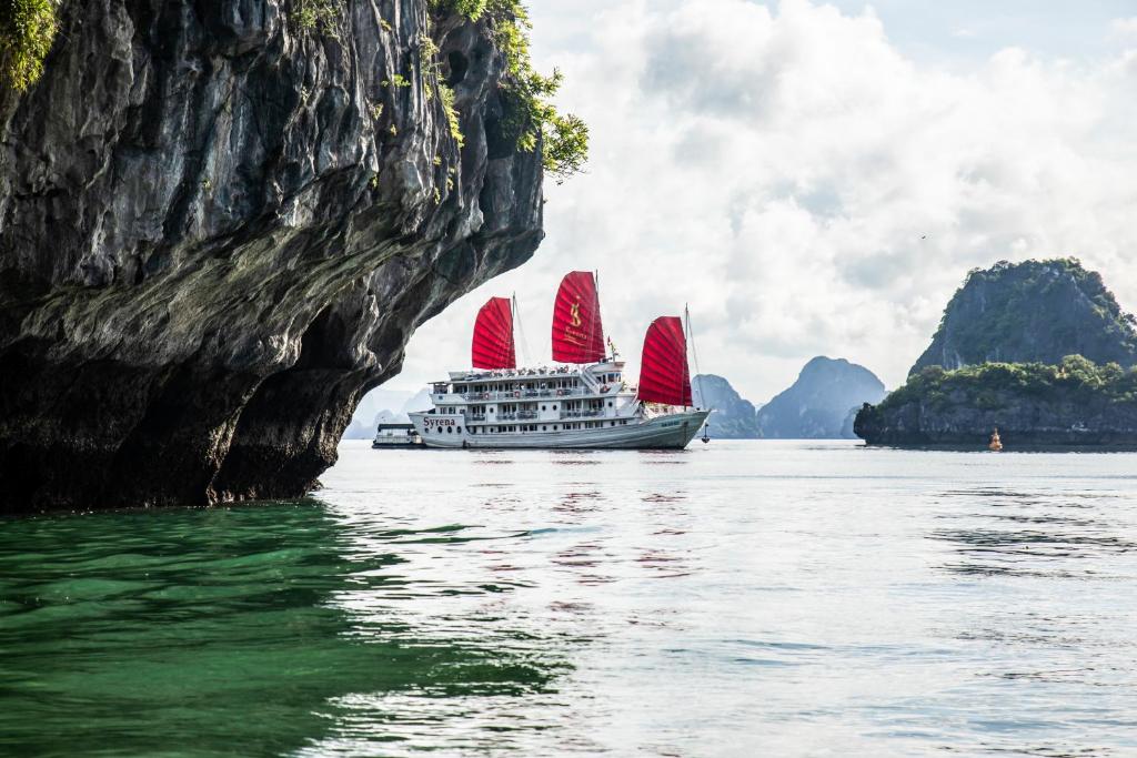 下龙湾美人鱼号邮轮酒店的船在岩石层附近的水中装有红色帆