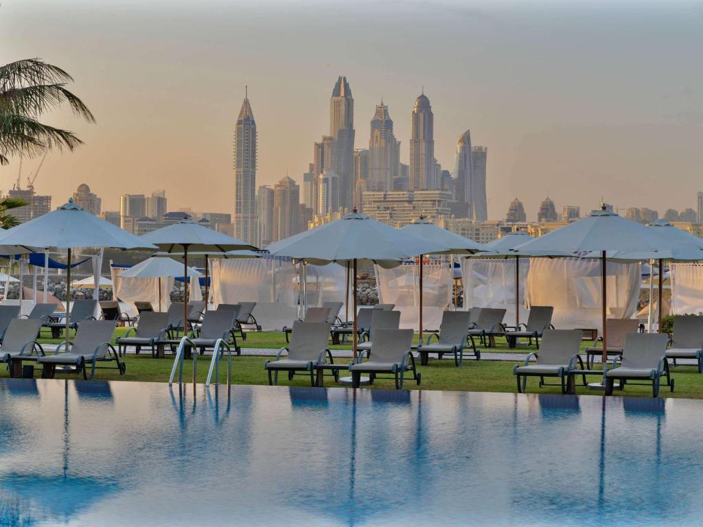 迪拜Rixos The Palm Luxury Suite Collection - Ultra All Inclusive的一个带椅子和遮阳伞的游泳池,并享有城市天际线